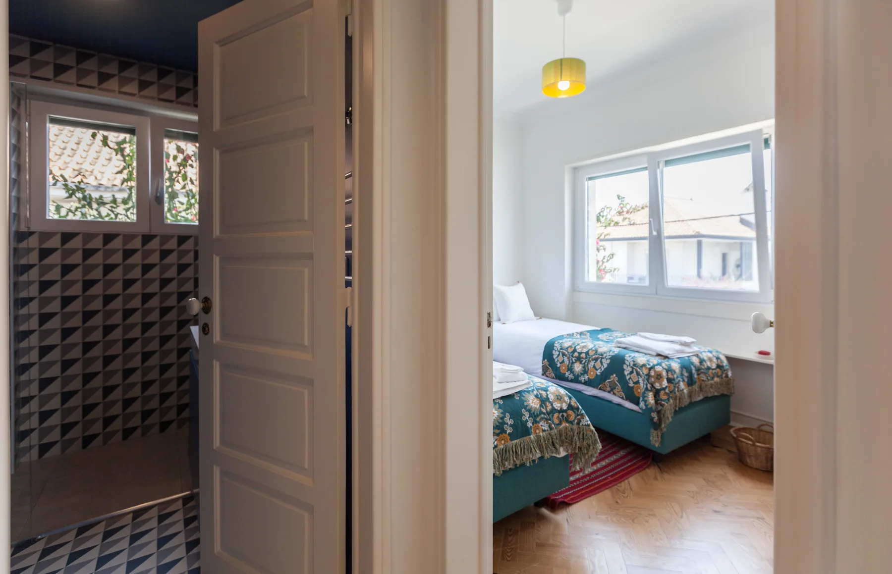 Dormitorio con dos camas y una ventana, junto a un baño con azulejos.