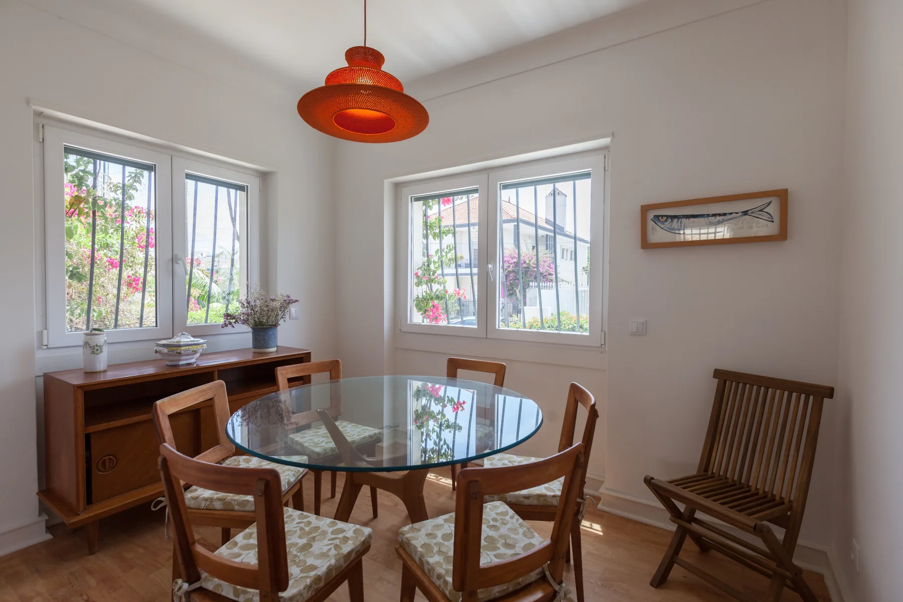 Un comedor con una mesa de vidrio y asientos de madera junto a ventanas luminosas.