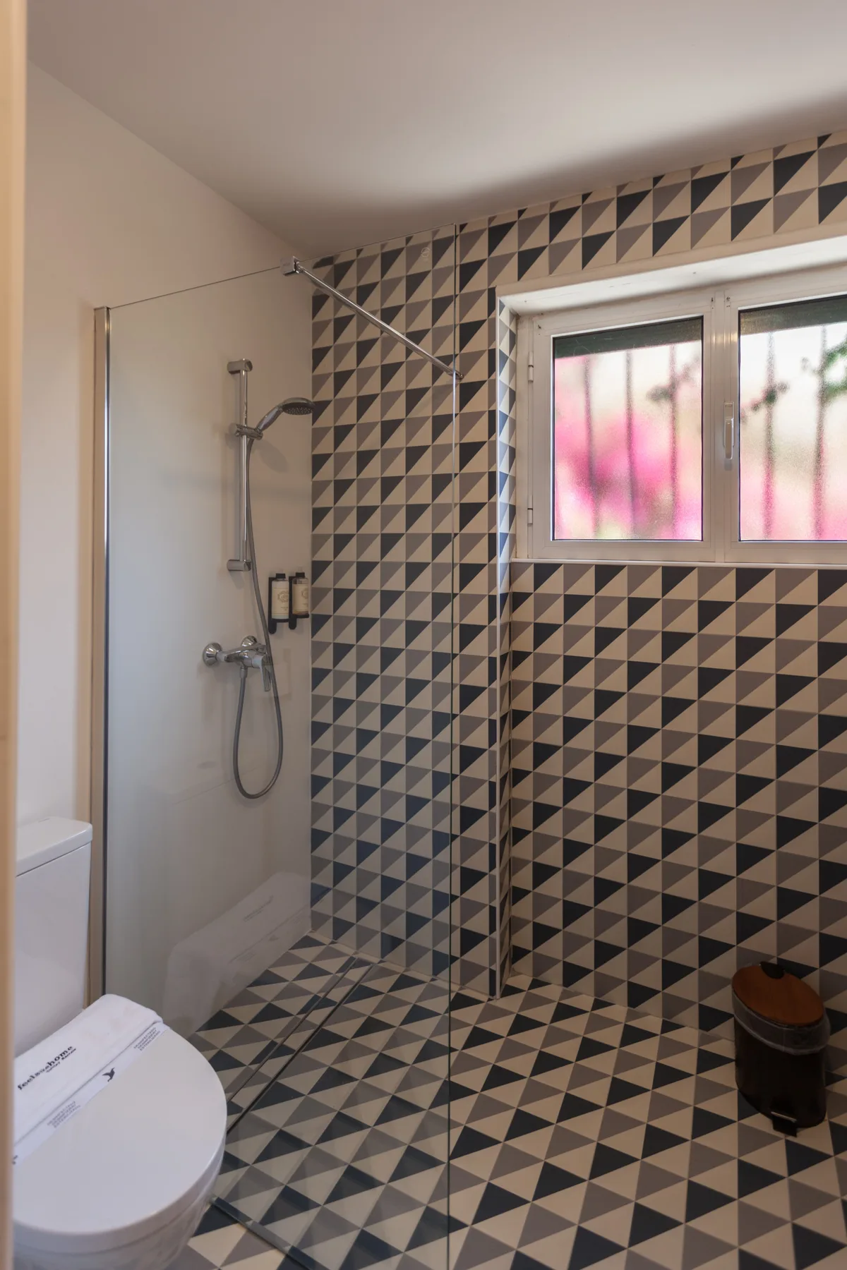 Un baño con ducha, inodoro y azulejos estampados.