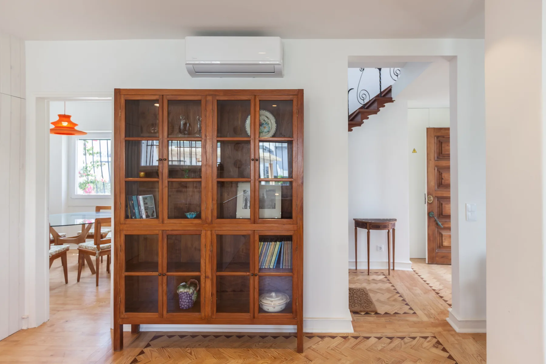 Un pasillo interior luminoso tiene un armario de madera con puertas de vidrio y suelo de parquet.