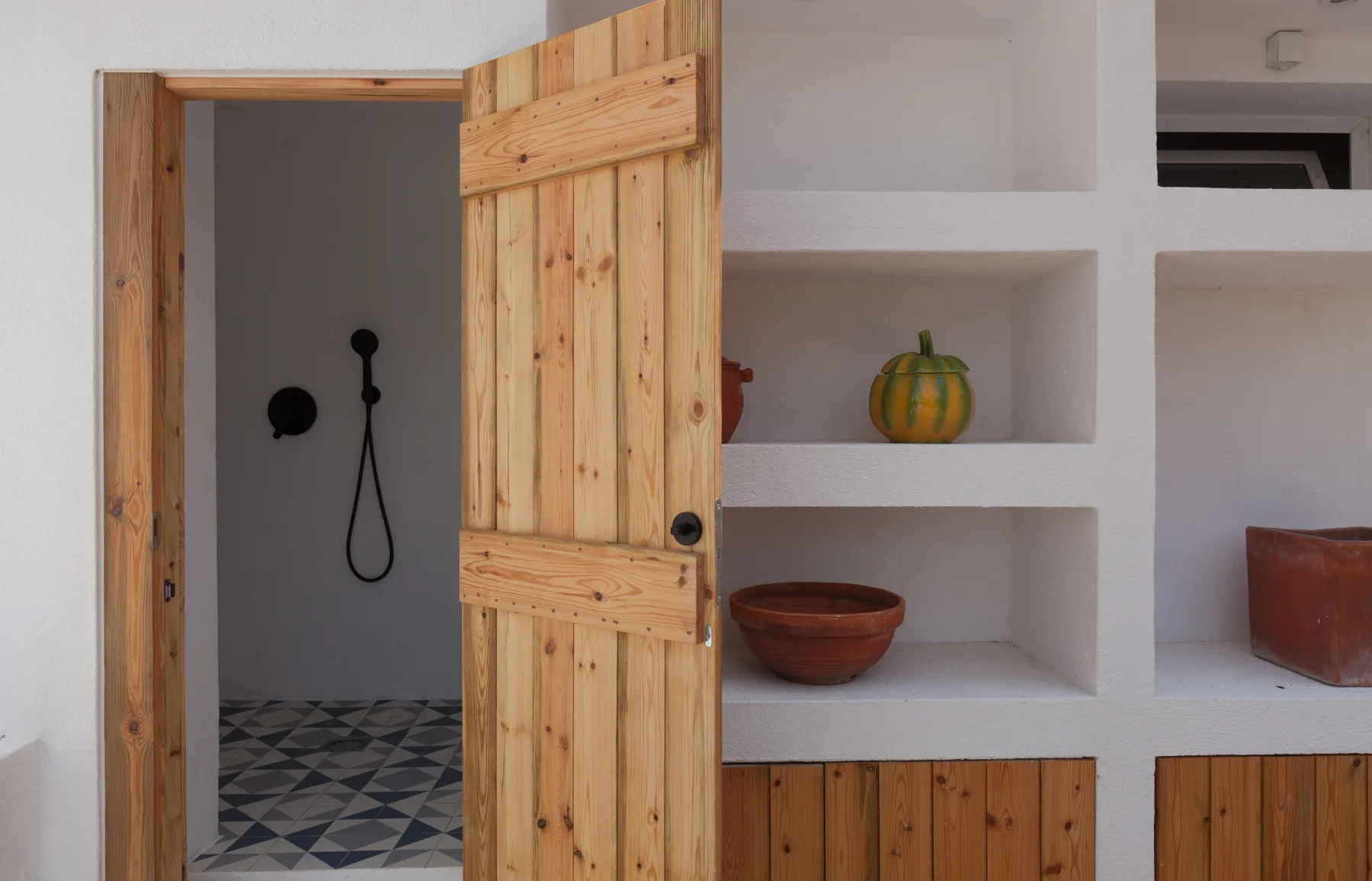 Una puerta de madera se abre junto a estantes empotrados con cerámica.