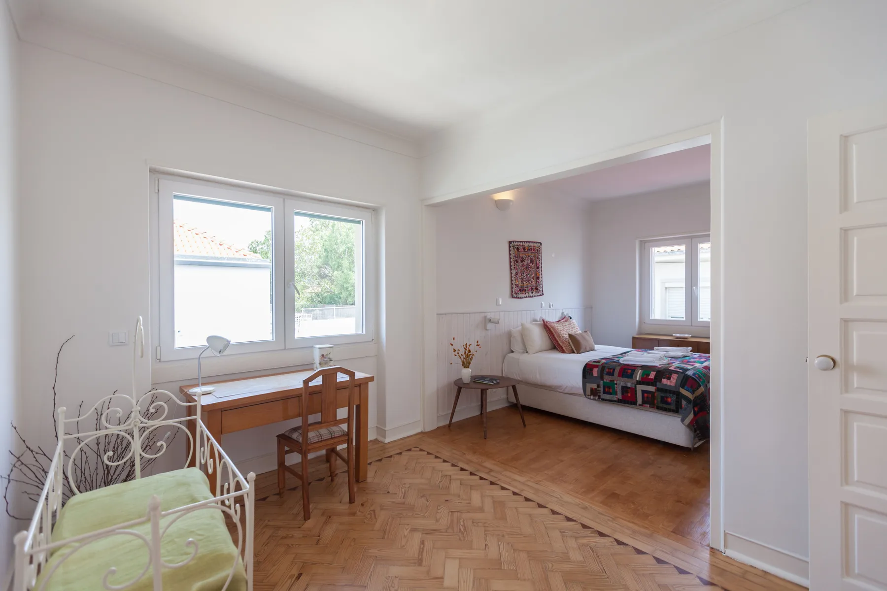 Un dormitorio luminoso con una cama, un escritorio pequeño y suelo de parqué.