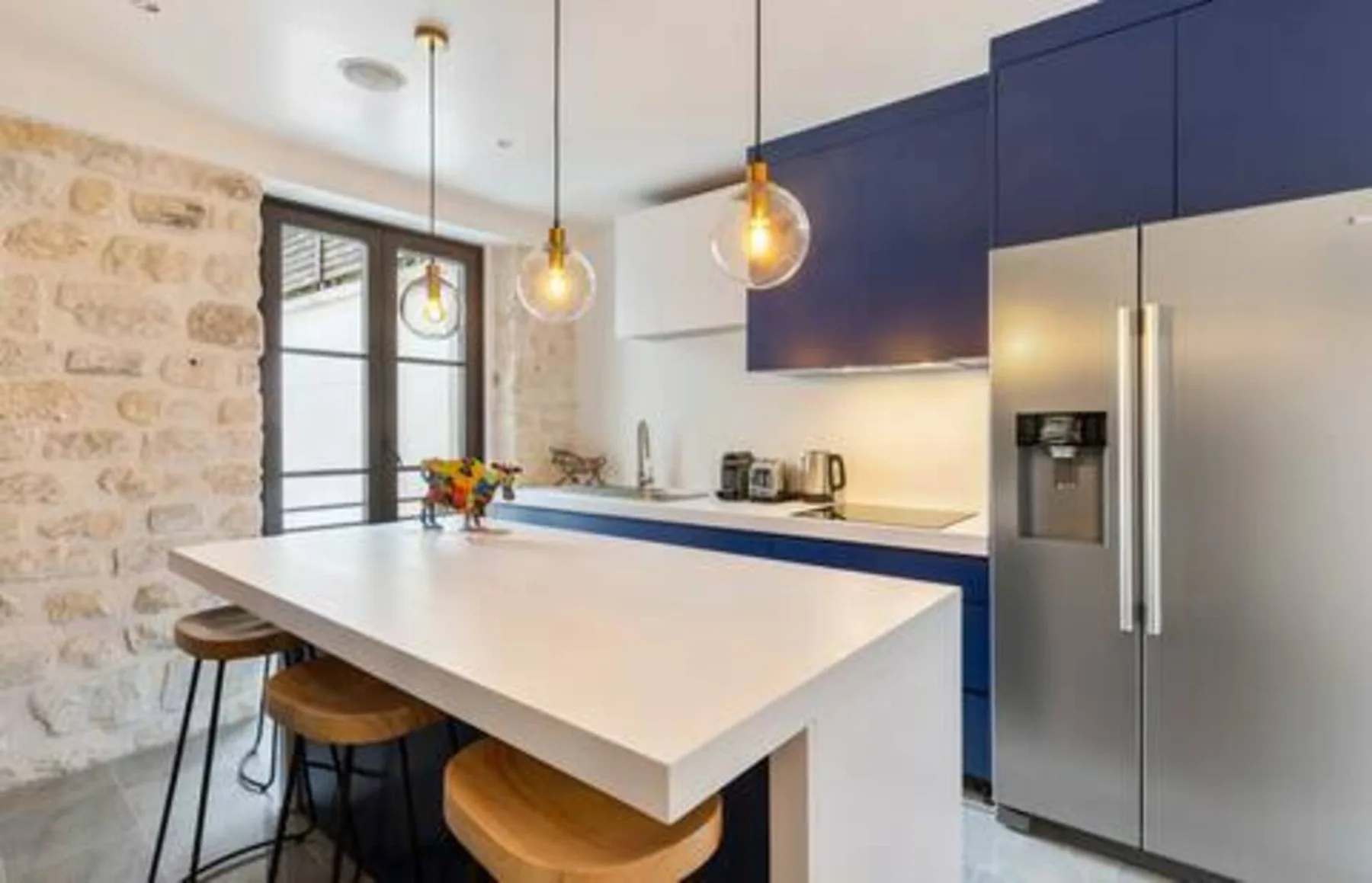 A modern kitchen with a large island, blue cabinetry, and pendant lights.