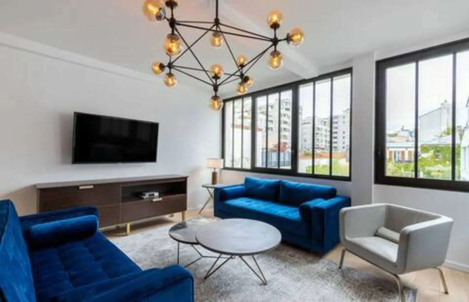A bright living room with blue seating, a television, and large windows.