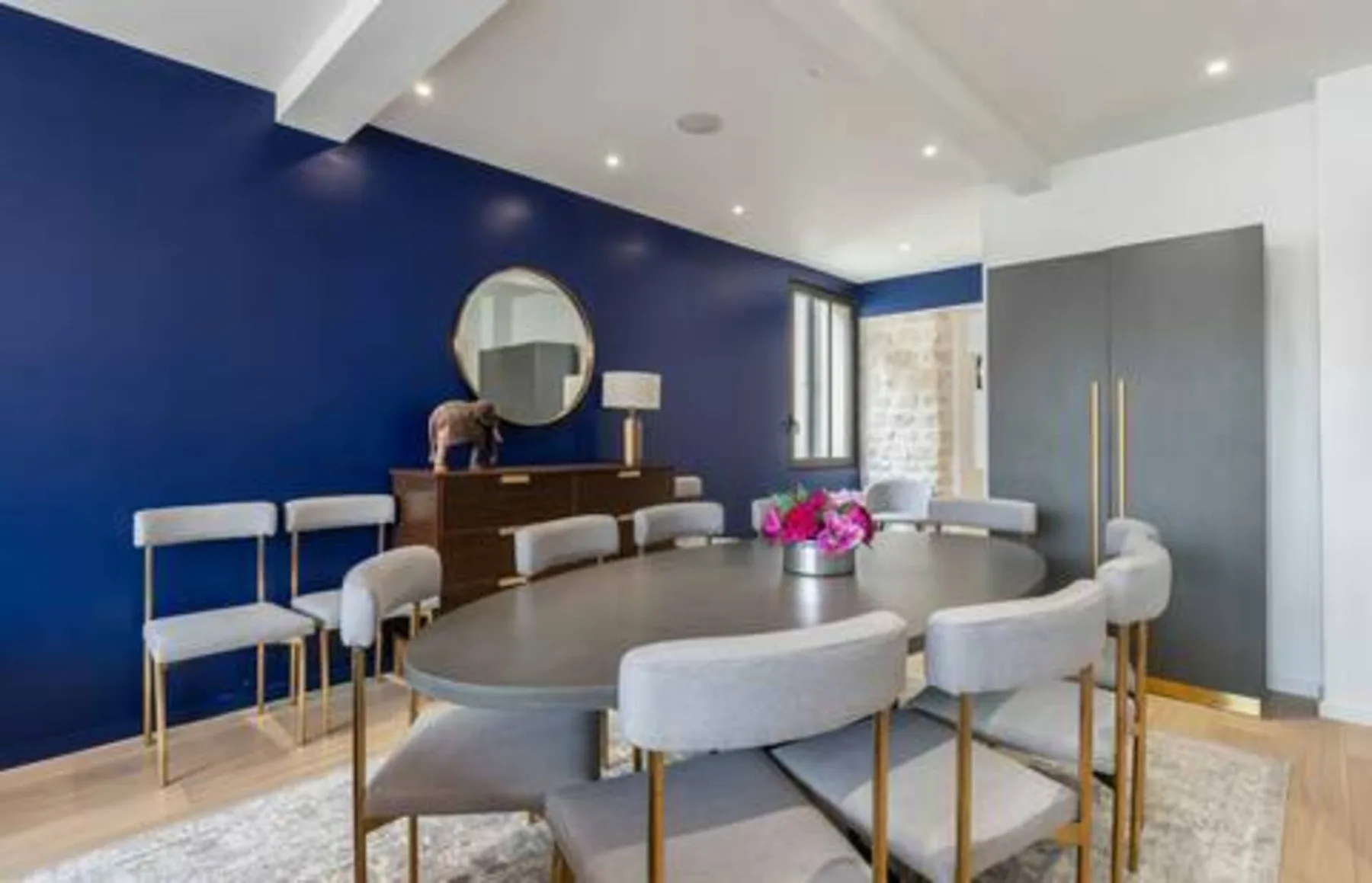 A dining area with a long table and upholstered seating against a blue wall.