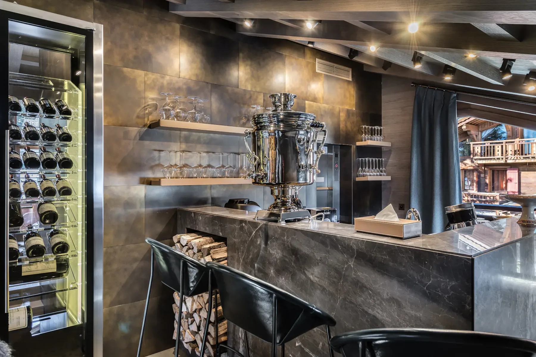 Interior de bar con una barra oscura, asientos y un expositor de vinos con frente de cristal.