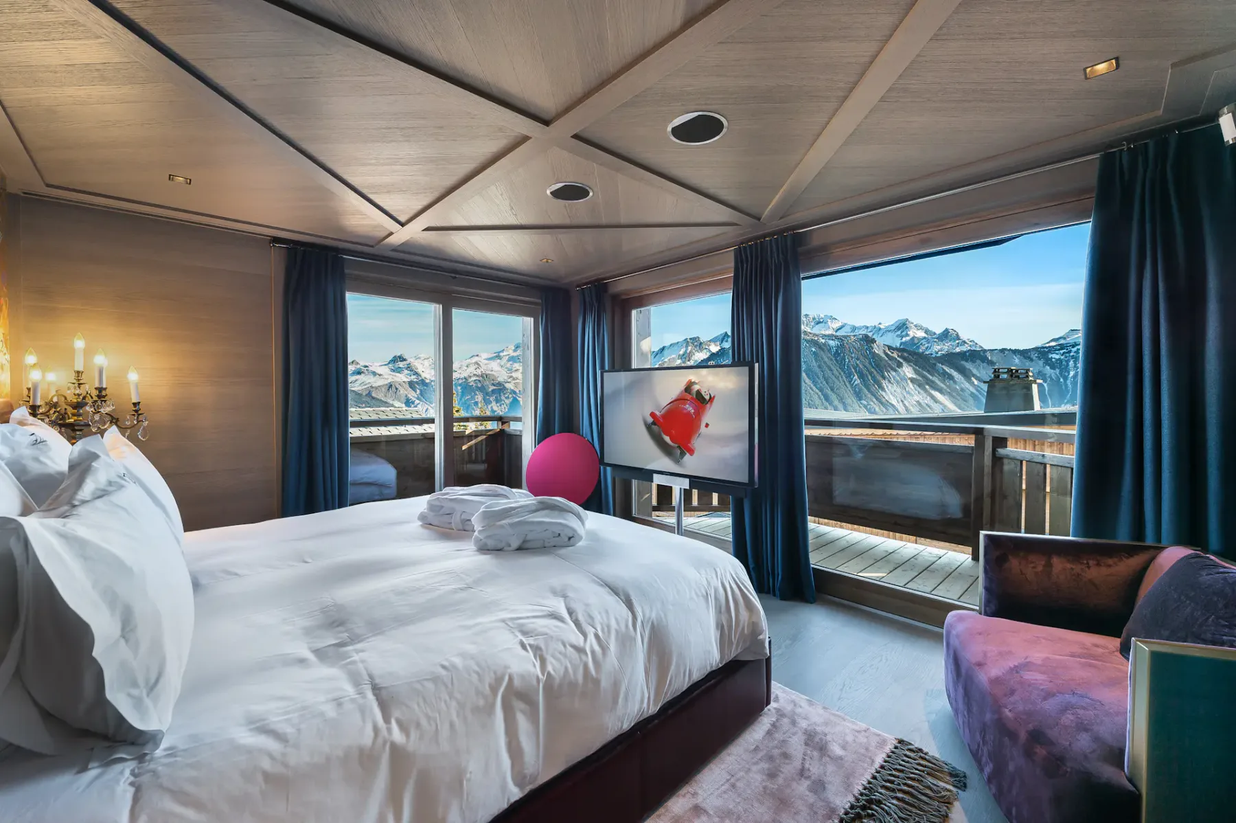 Dormitorio con una cama grande, un televisor y vistas a las montañas a través de ventanas que dan a un balcón.