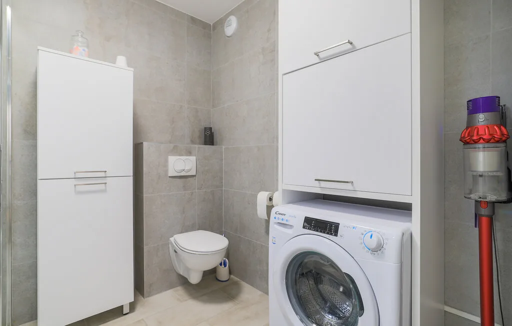 A tiled bathroom with a wall-mounted toilet and a washing machine.