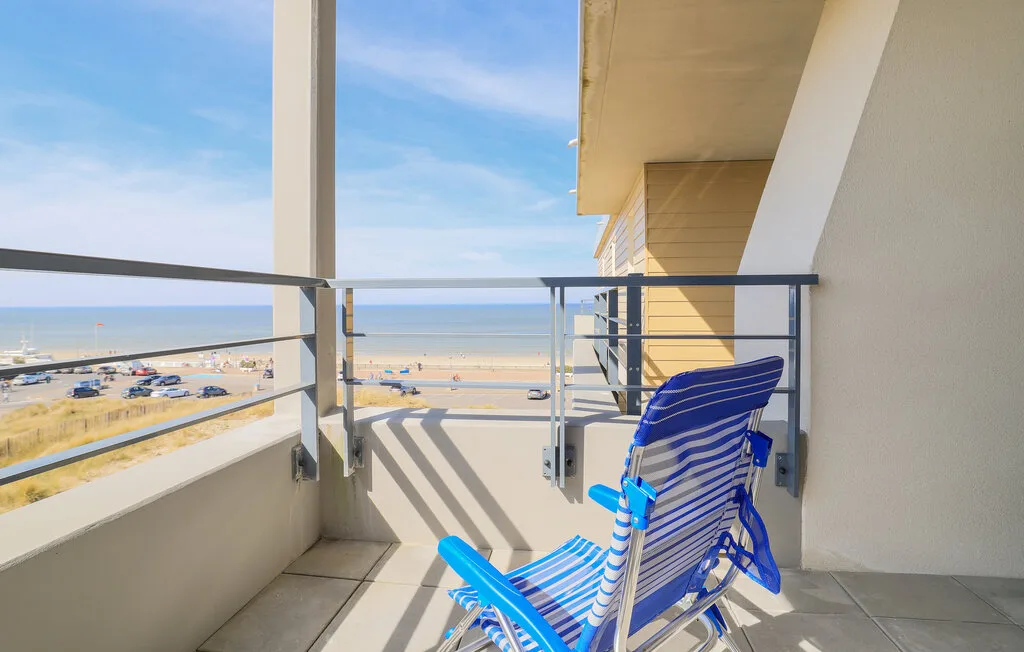 A balcony with a striped folding chair overlooks the beach and ocean.
