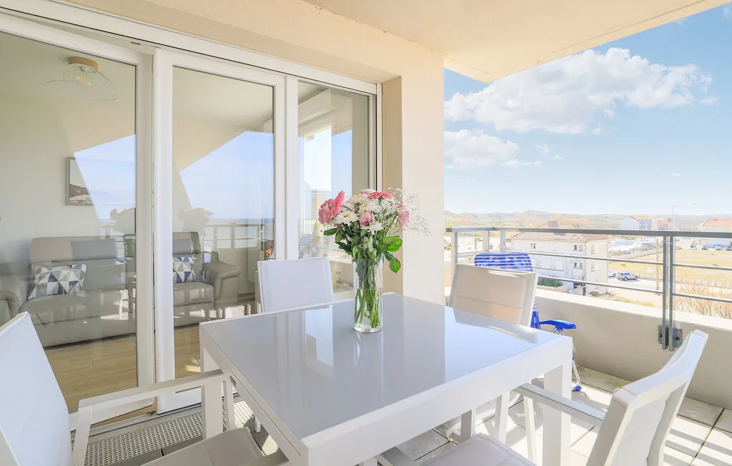 Comedor en un balcón con una mesa y flores junto a puertas corredizas de vidrio.