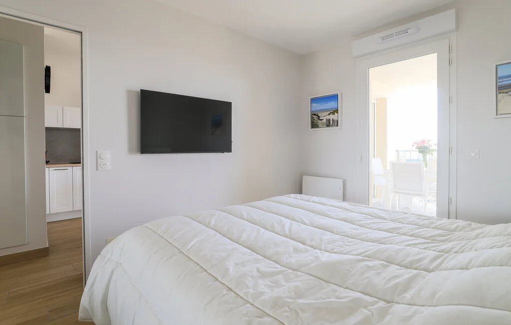 A bedroom with a white bed and a television mounted on the wall.