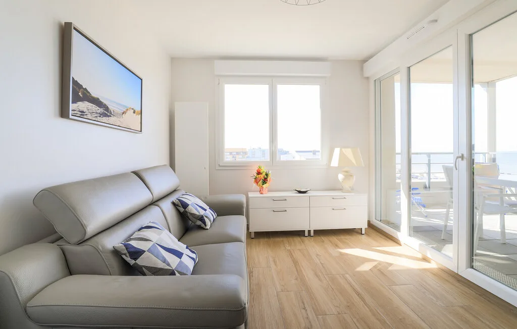 A bright living room with seating beside large windows opening onto a balcony.