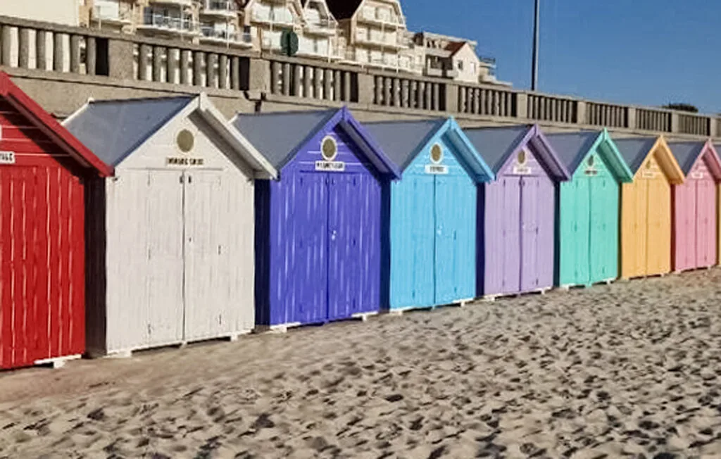 A row of brightly painted beach huts stands beside a sandy beach.