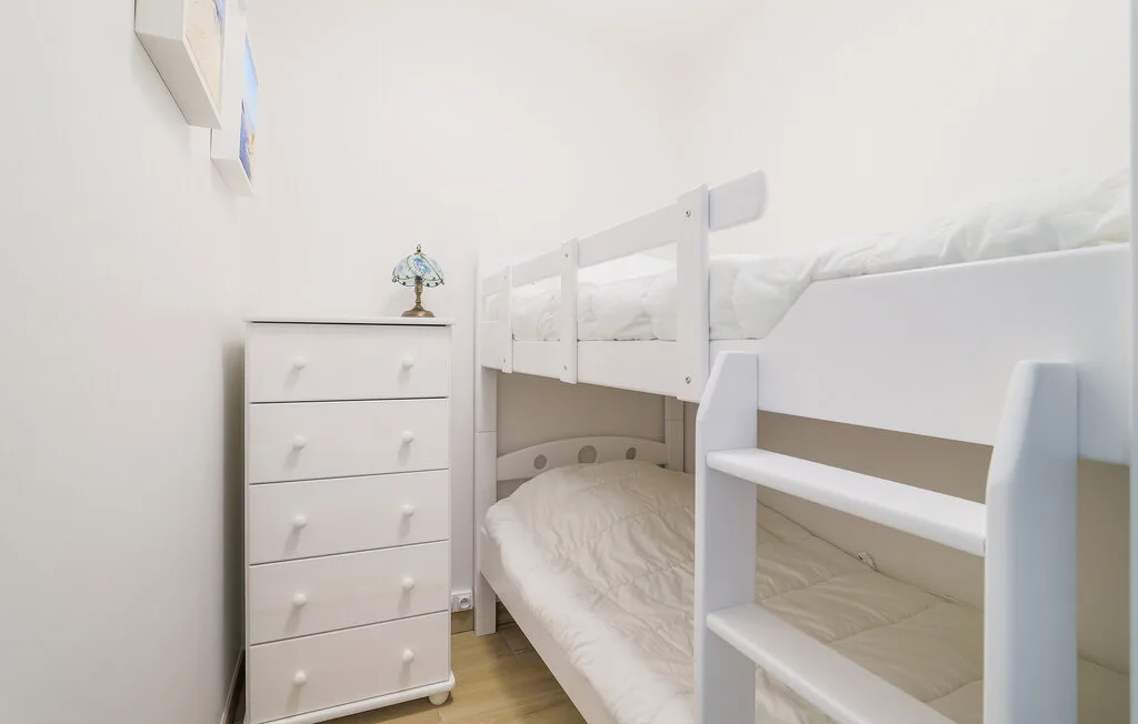 A bright bedroom with a white bunk bed and a chest of drawers.