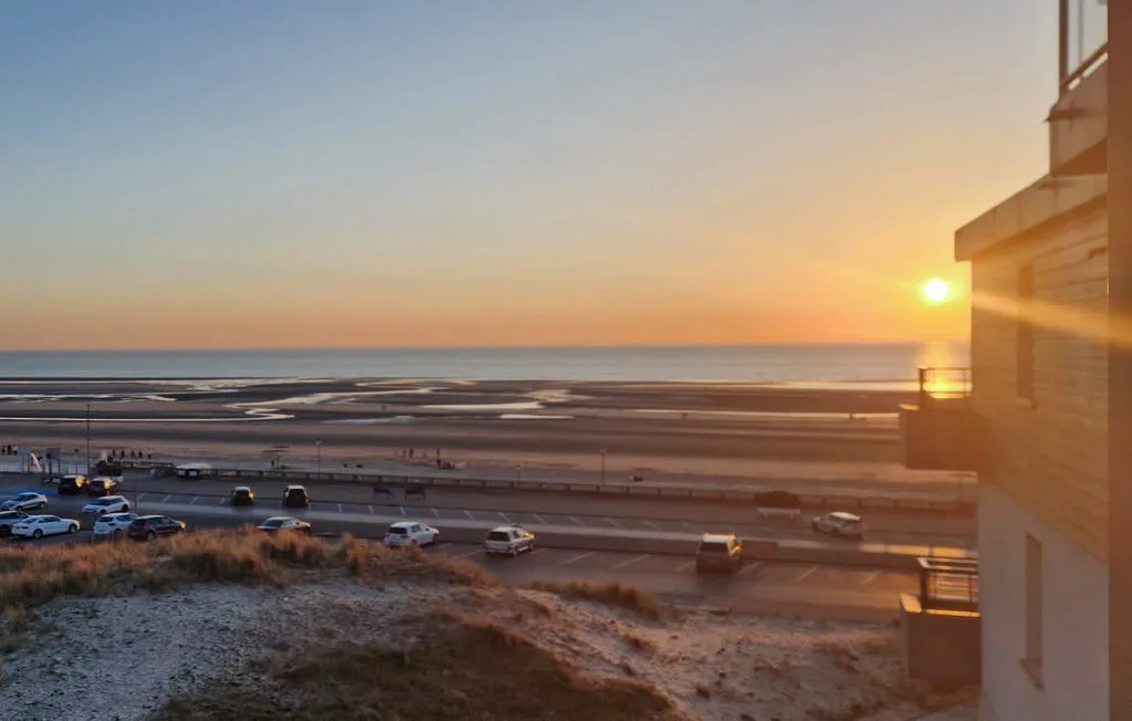 Sunset over the ocean, with a coastal road and buildings in the foreground.