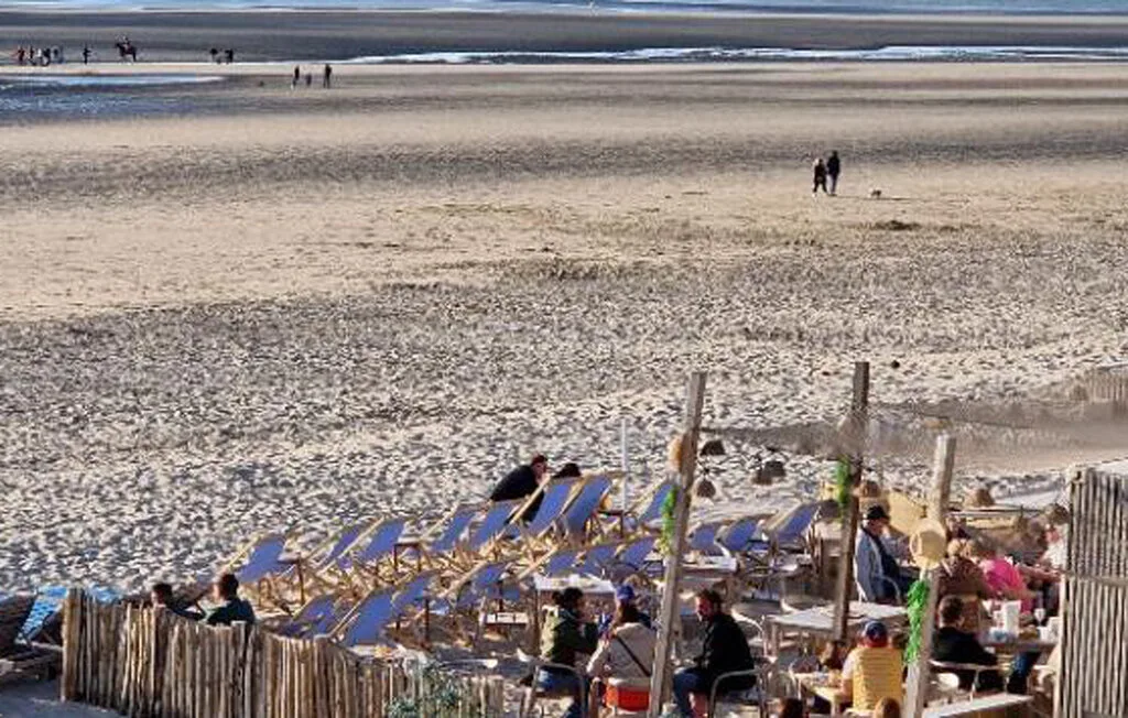 A sandy beach with people seated among beach chairs near the shoreline.