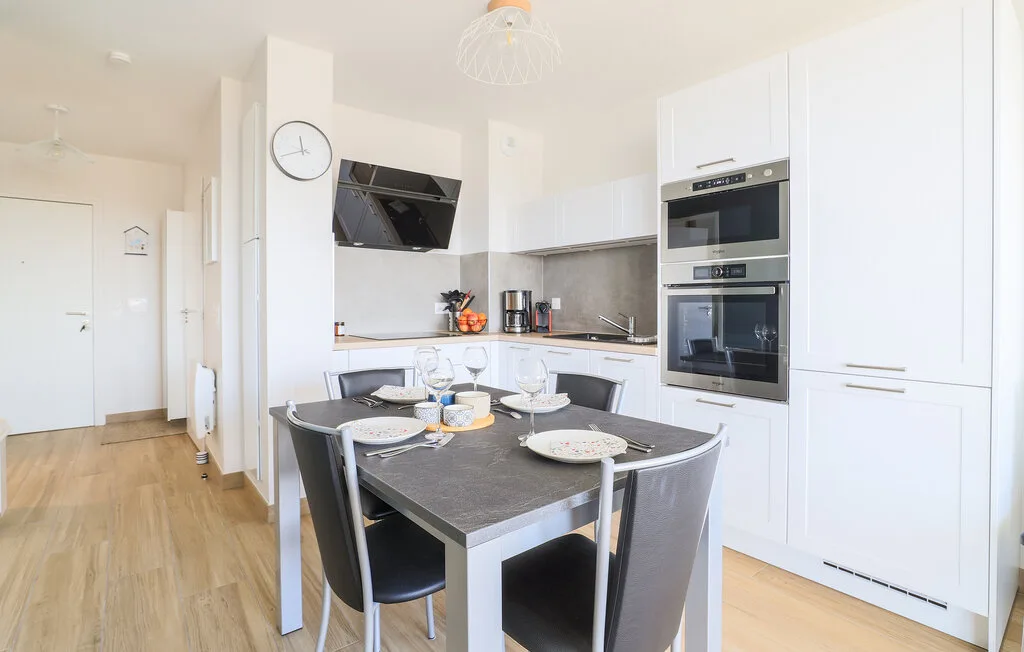 Una cocina luminosa con zona de comedor, armarios blancos y una mesa.