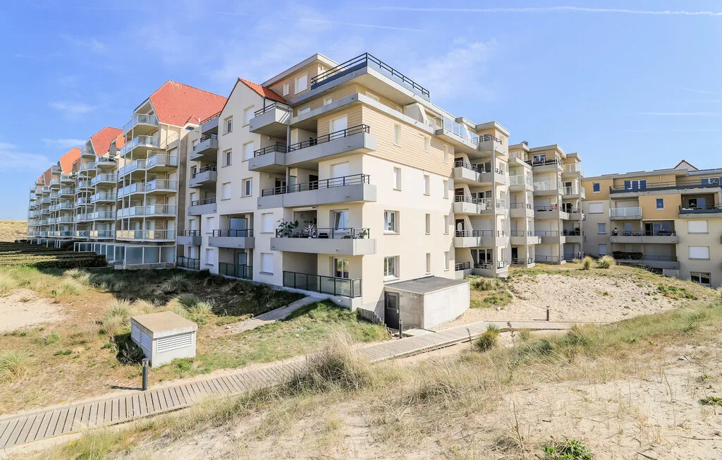 Apartment buildings with balconies stand beside a sandy coastal path.