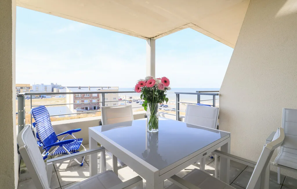 A balcony dining area with a table, seating, and flowers overlooking the sea.