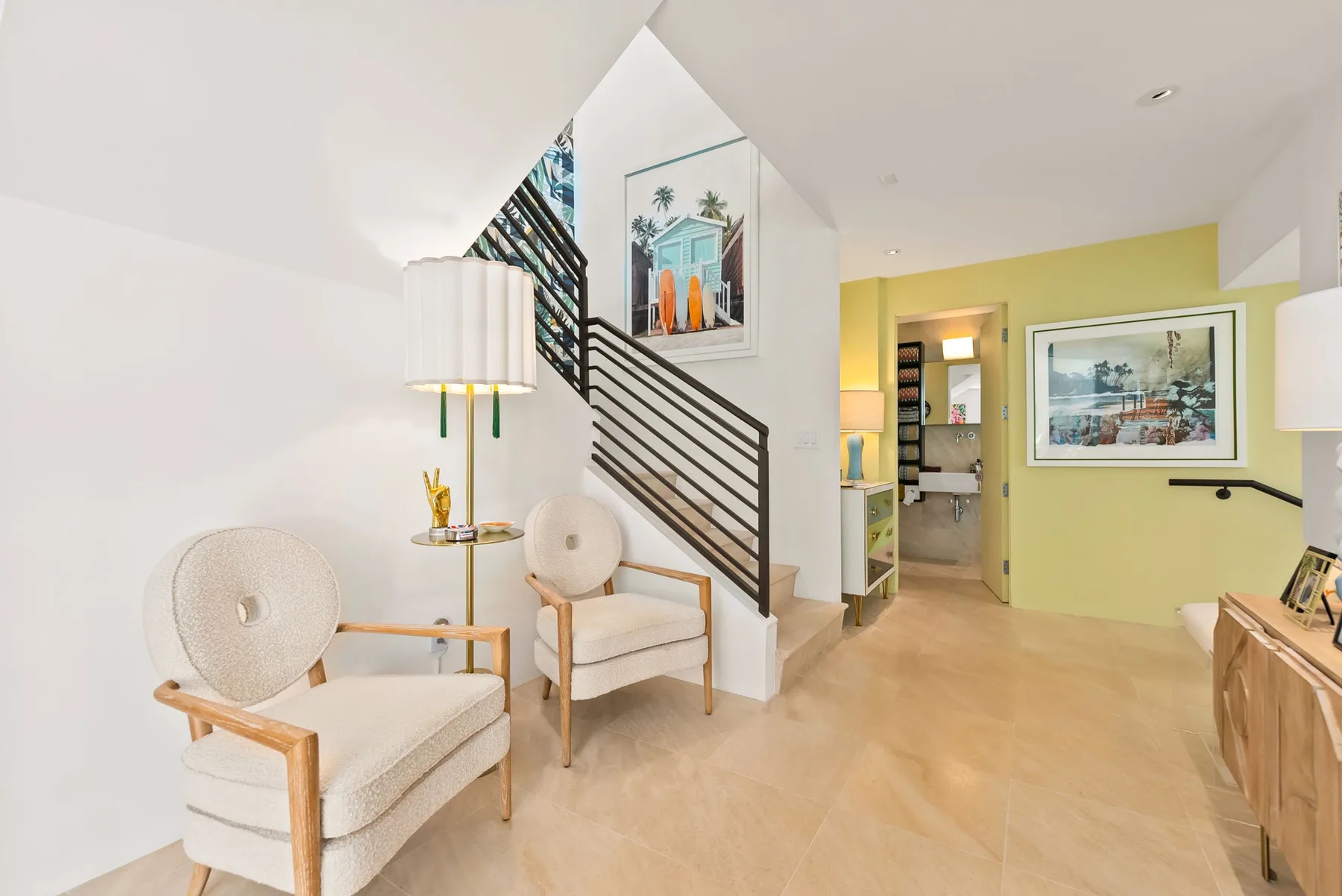 A bright living area with seating beside a staircase and framed artwork.