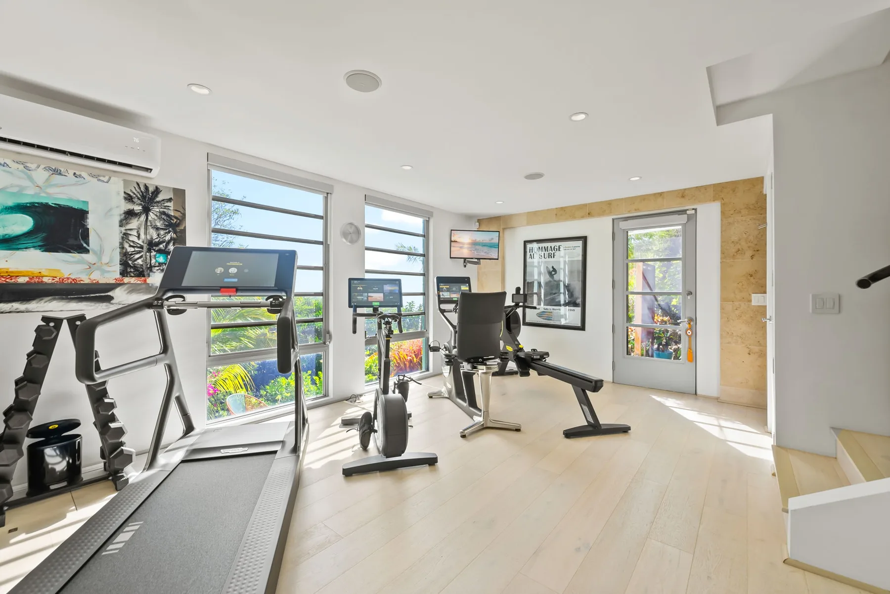 A bright home gym with exercise equipment beside large windows.