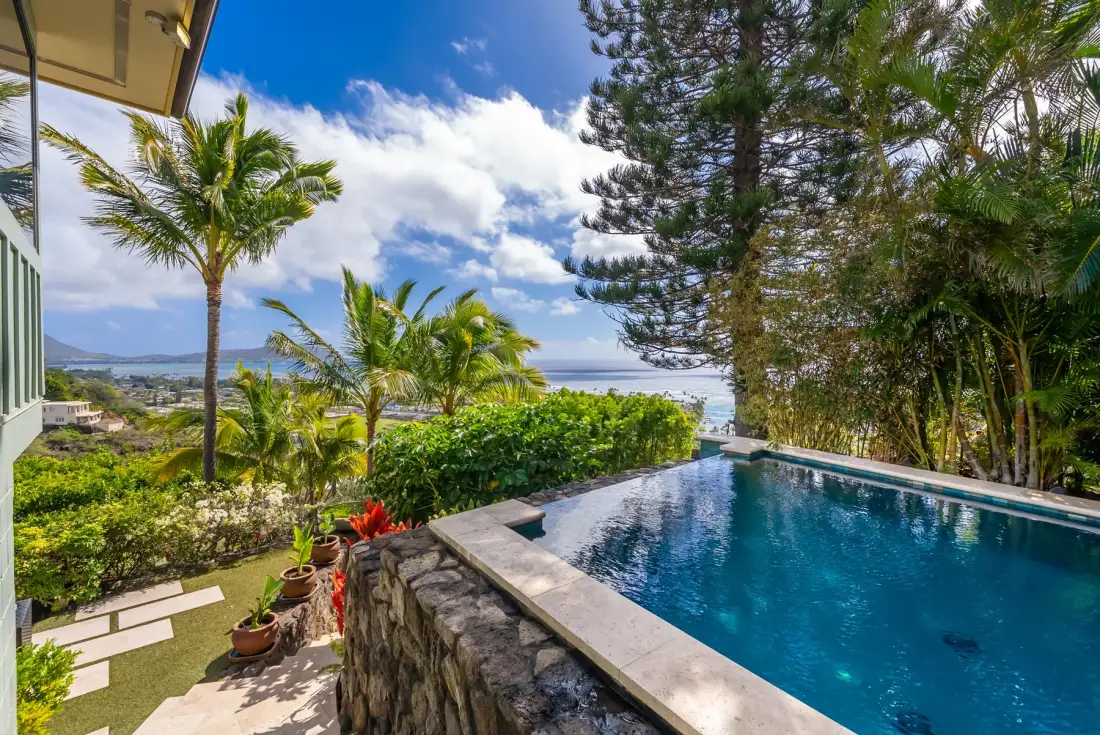 An outdoor swimming pool overlooks lush tropical greenery and the ocean.