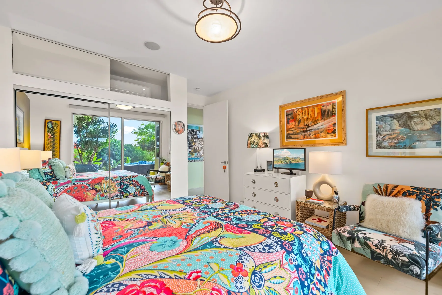 A colorful bedroom with a patterned bedspread and a sitting area by the window.