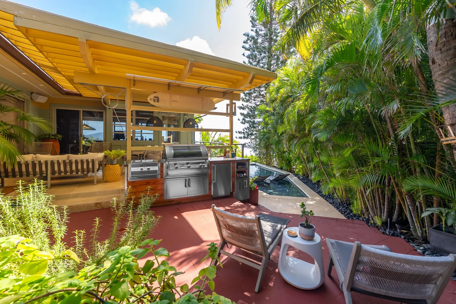 An outdoor patio with a covered grill area and seating beside a pool.