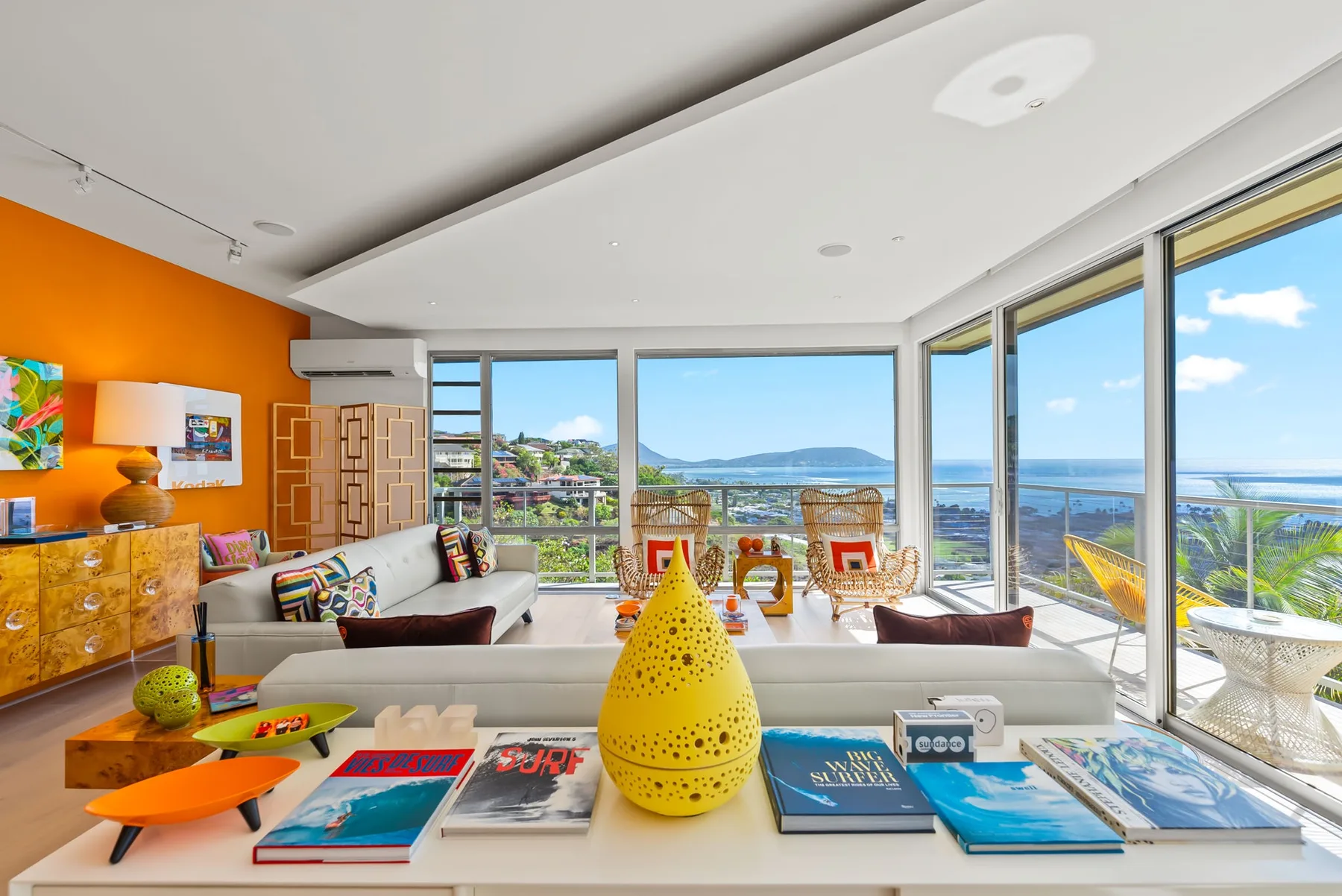 A bright living room with colorful furnishings and wide windows overlooking the ocean.