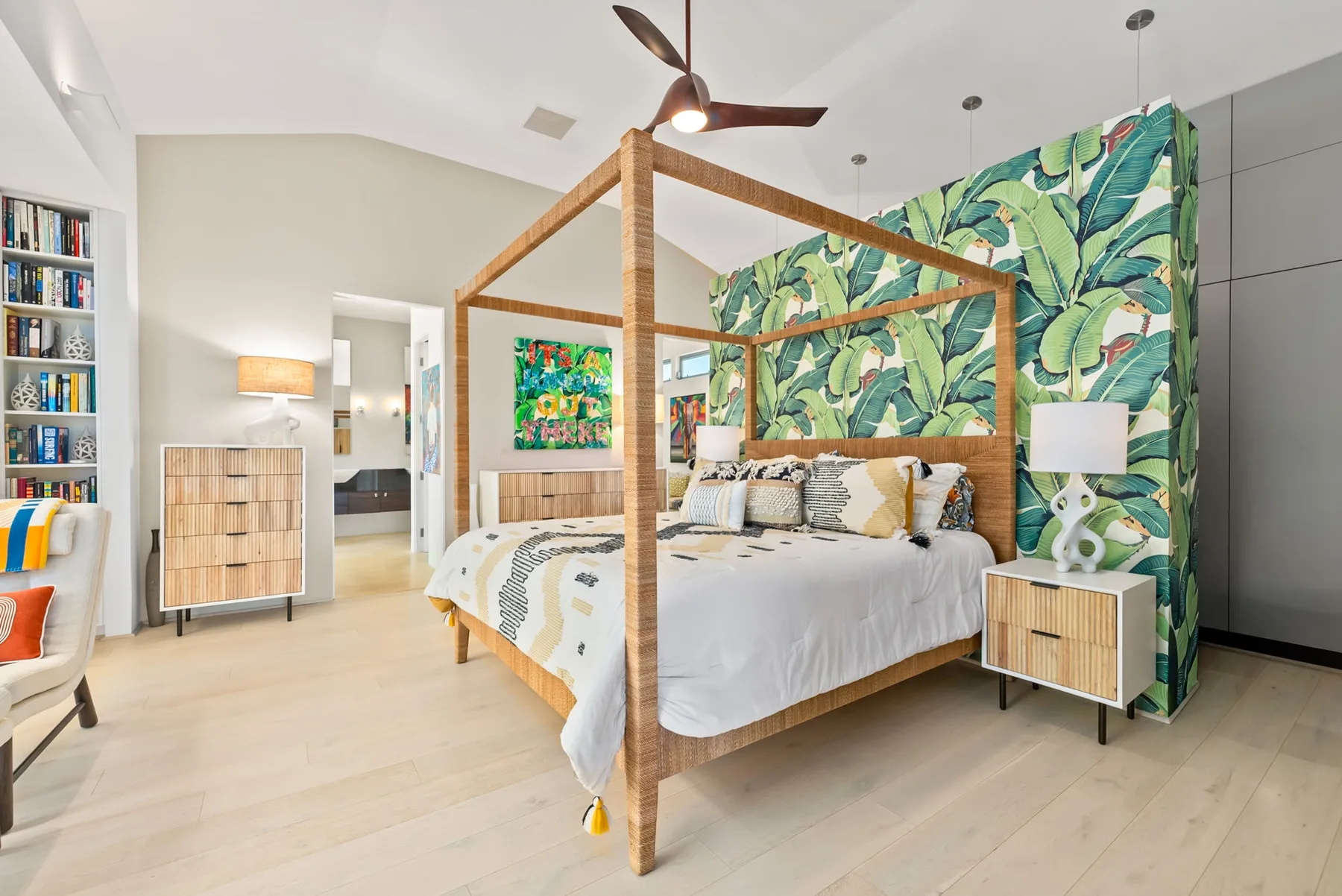 A bright bedroom features a canopy bed and a leafy patterned wall.