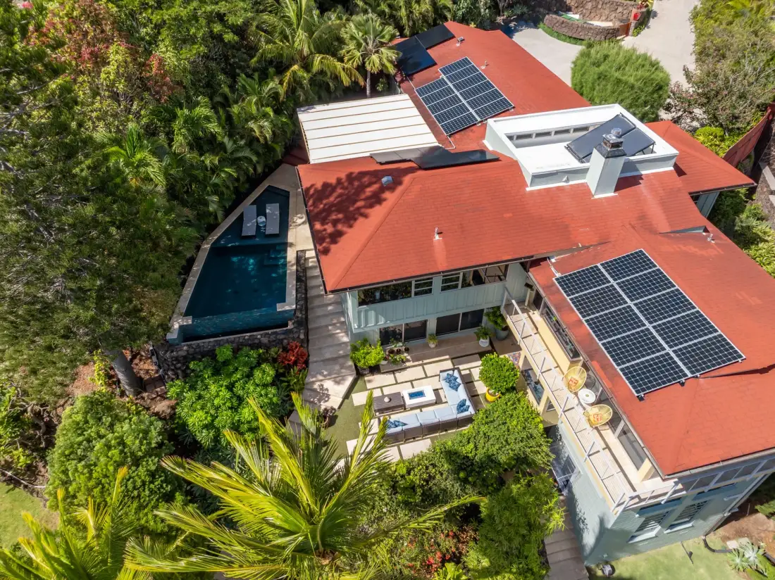 An aerial view of a red-roofed house with solar panels and a swimming pool.