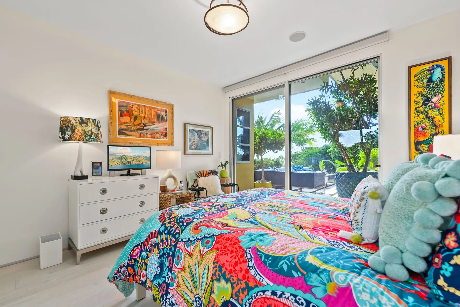 A colorful bedroom with a patterned bedspread beside large windows overlooking greenery.