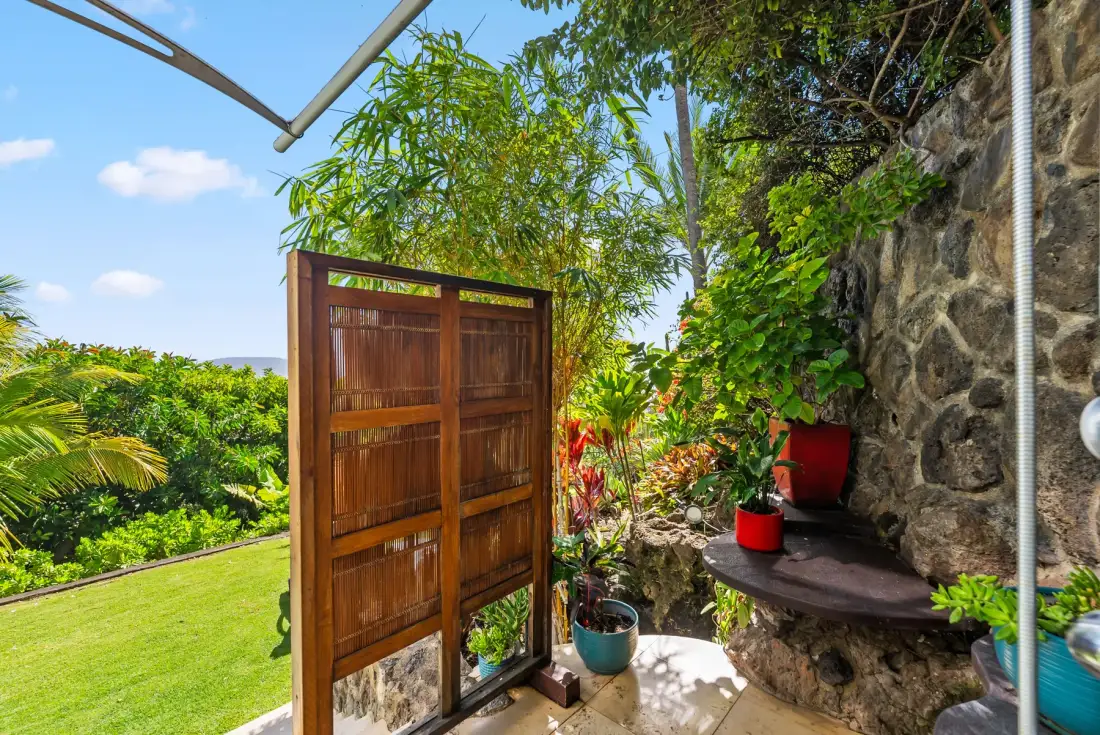 A garden patio features a wooden privacy screen, potted plants, and a stone wall.