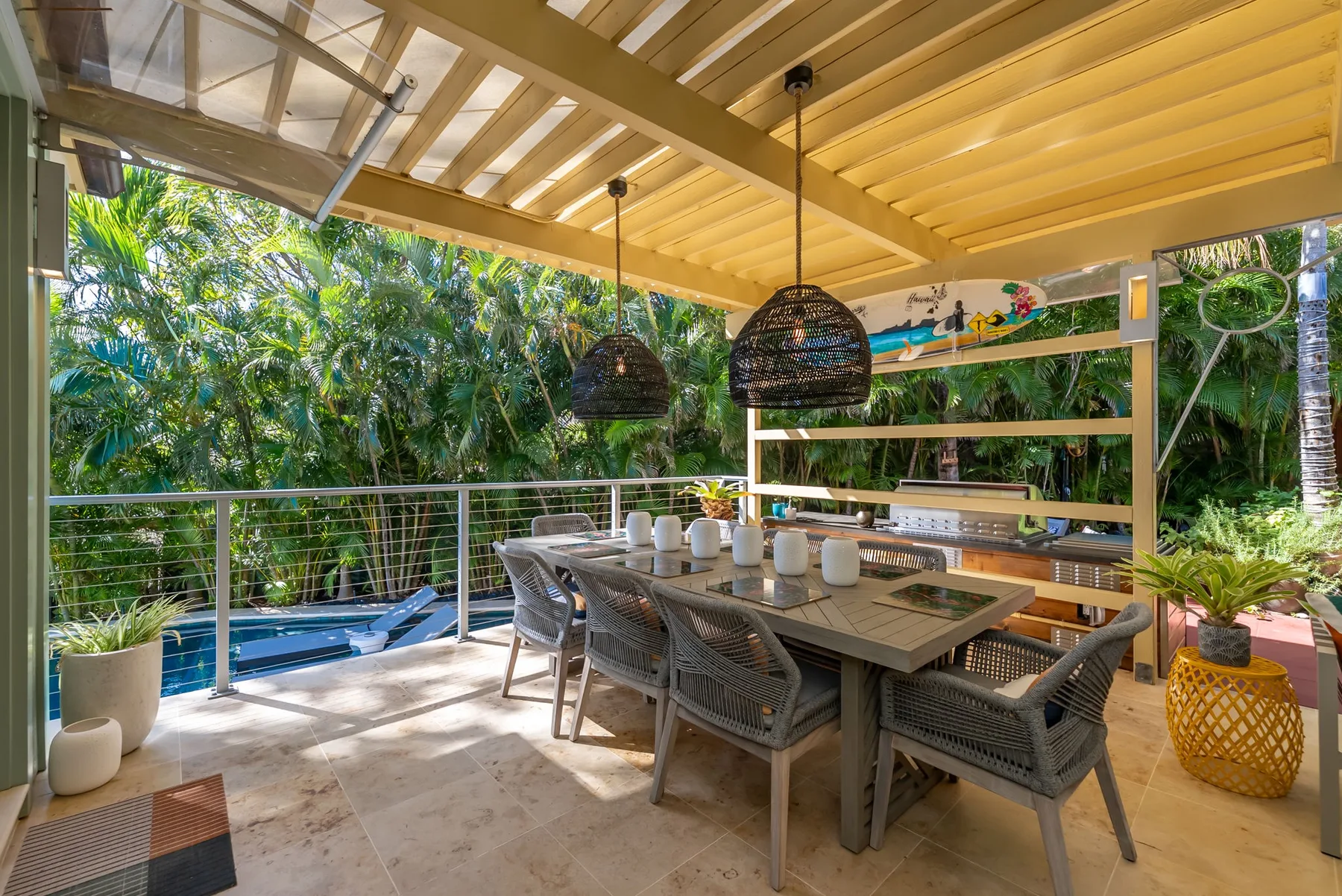 A covered outdoor dining area with a long table and surrounding greenery.