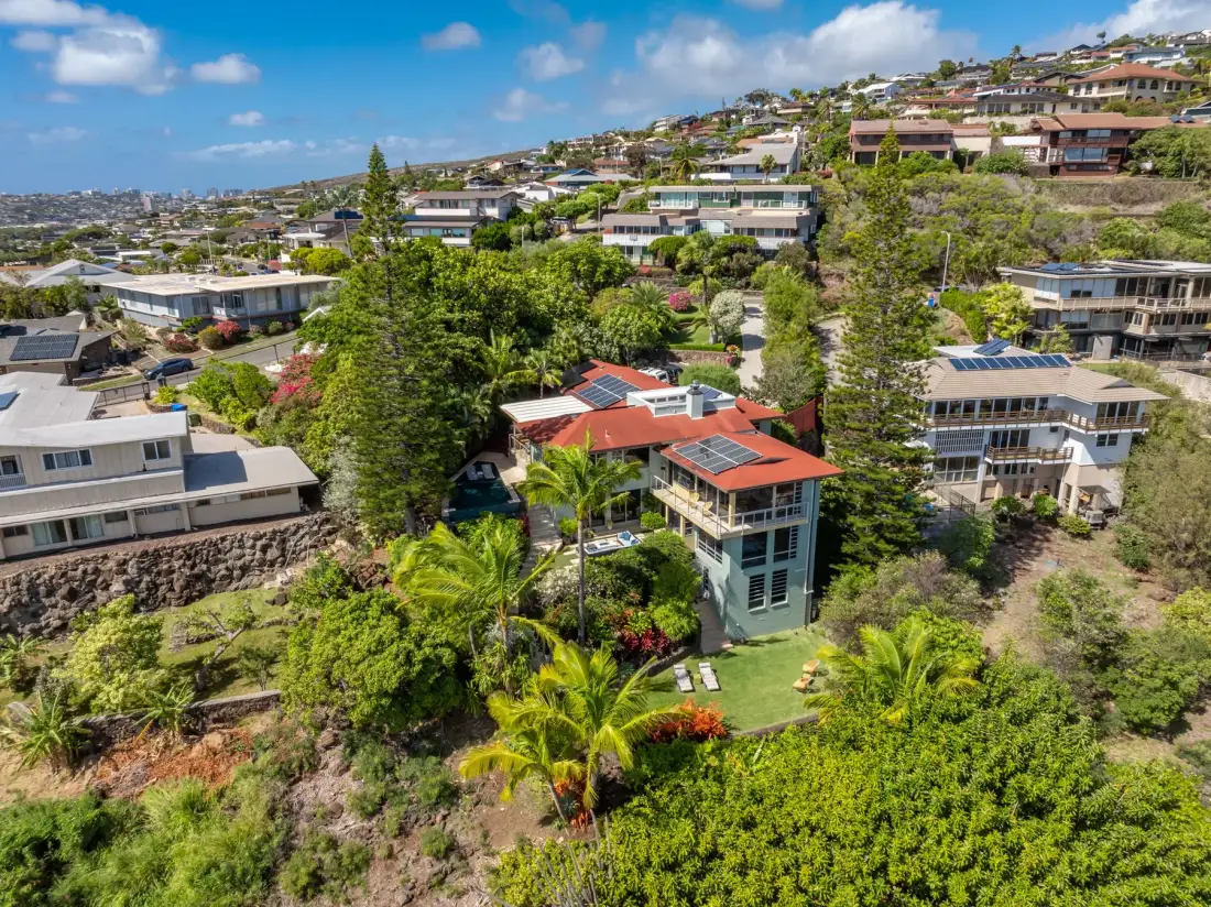 A hillside neighborhood of homes surrounded by green trees and gardens.