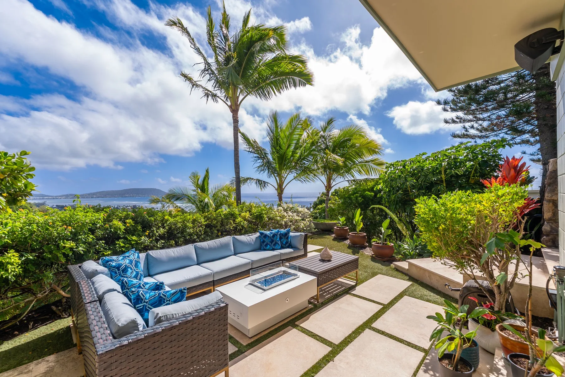 An outdoor patio with cushioned seating, potted plants, and a view of the water.