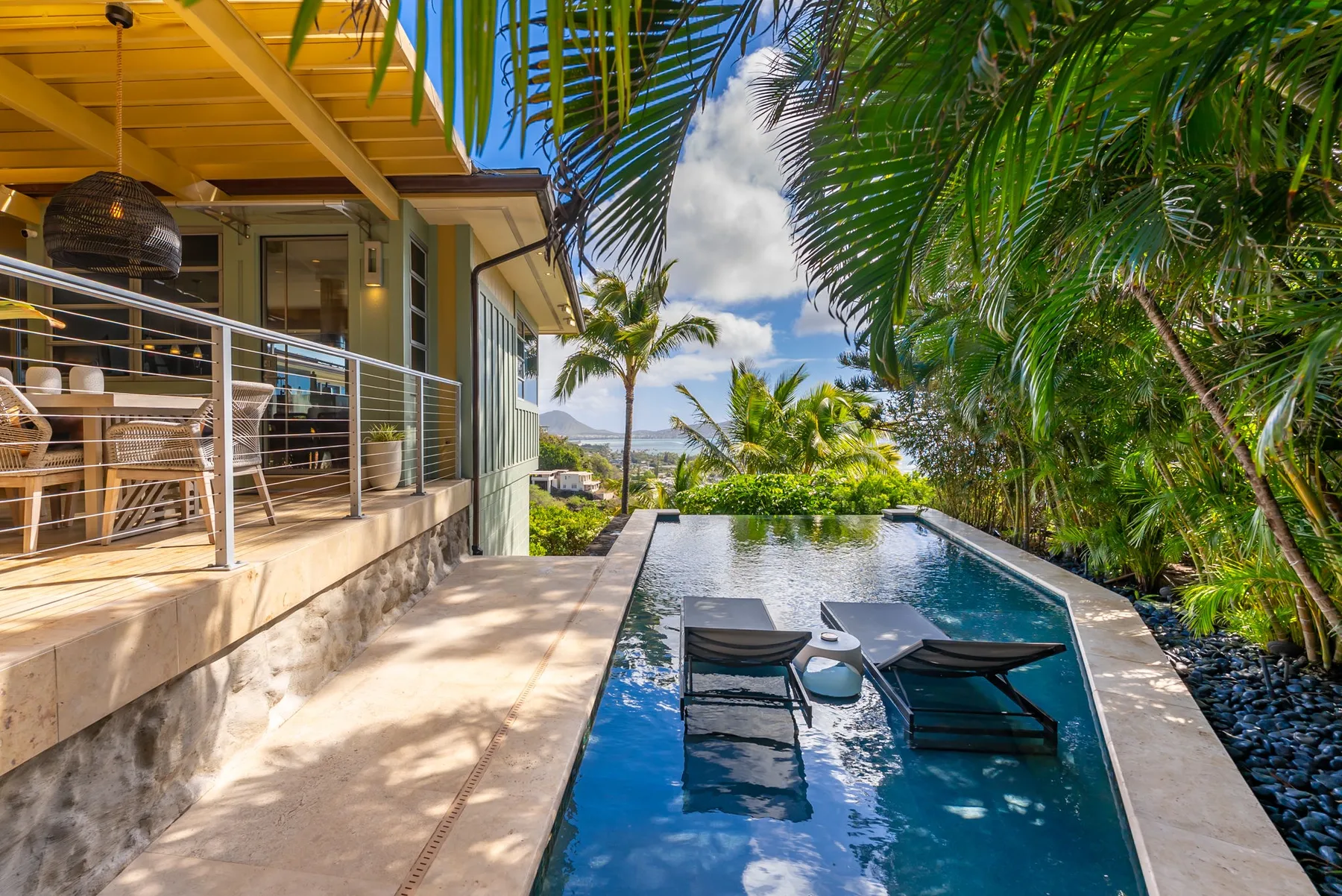 A tropical outdoor pool beside a covered patio, surrounded by lush palms.