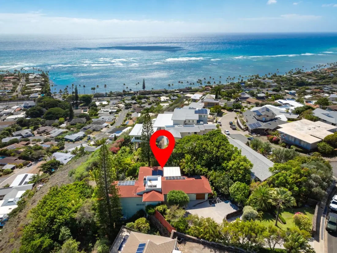 Aerial view of a coastal neighborhood with a red-roofed house and ocean beyond.