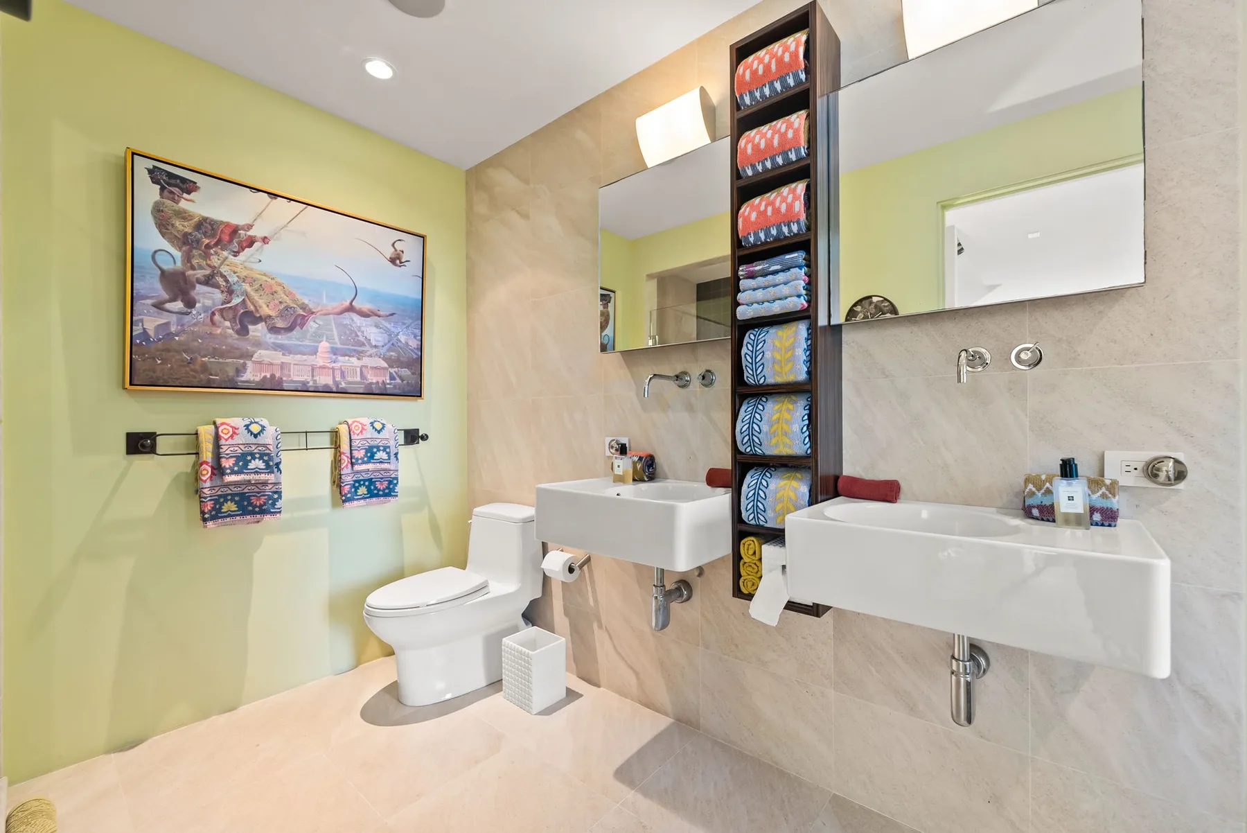 A bright bathroom with two sinks, a toilet, and colorful wall art.