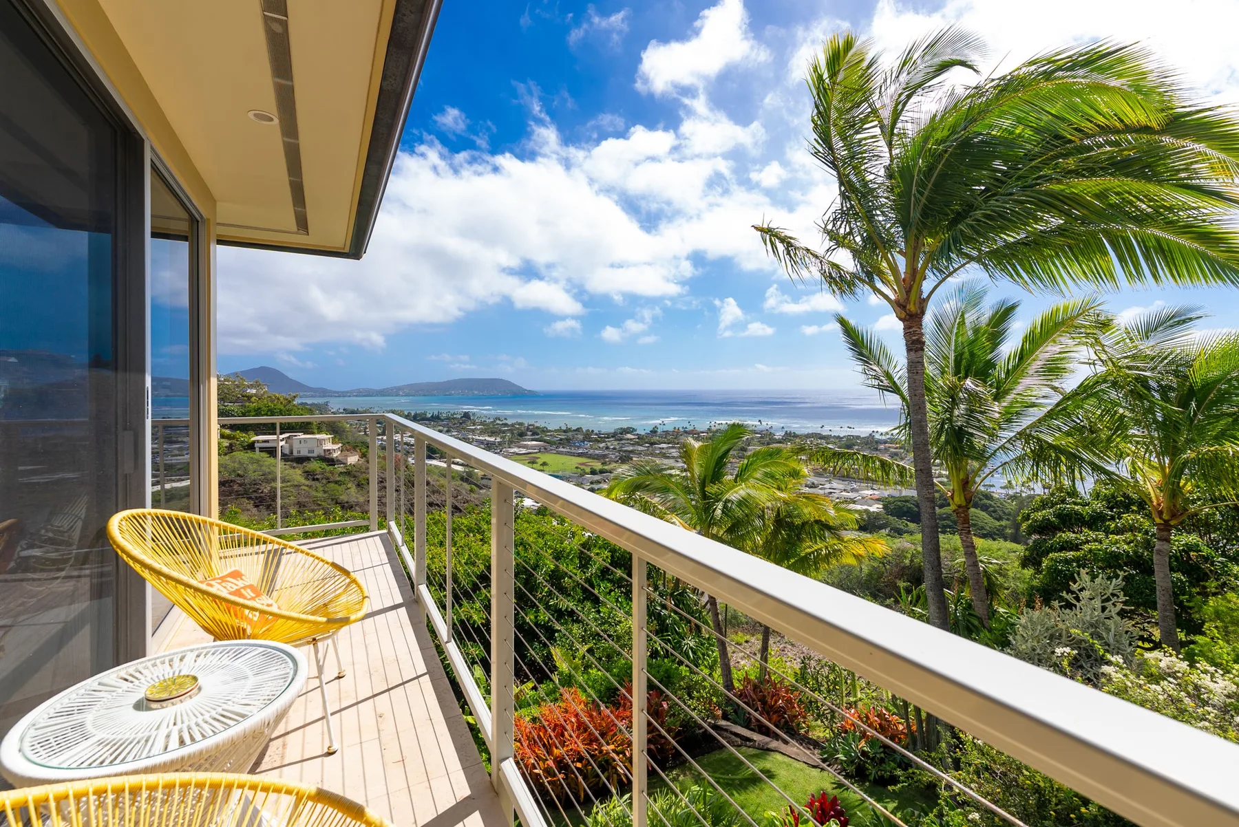 A balcony overlooks lush greenery and a distant coastline.