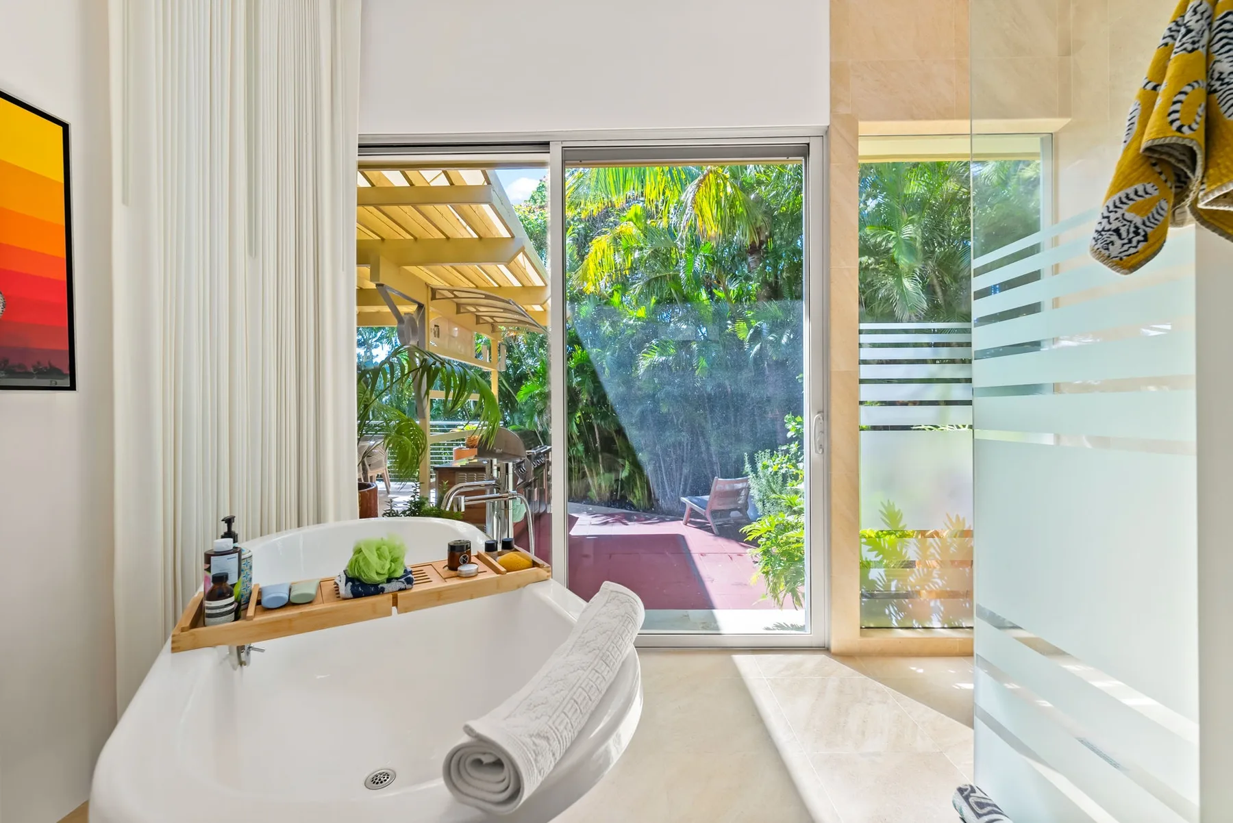 A bathroom with a bathtub beside glass doors opening onto a leafy patio.