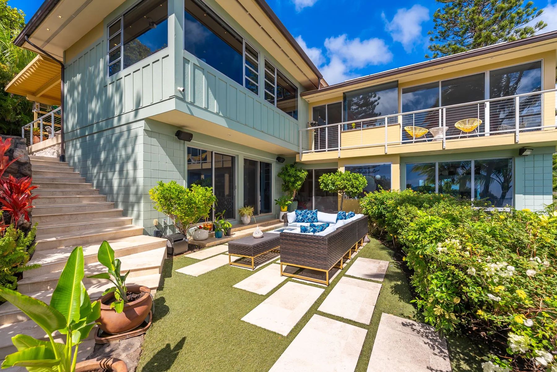 A modern house surrounds a patio with outdoor seating and a garden.