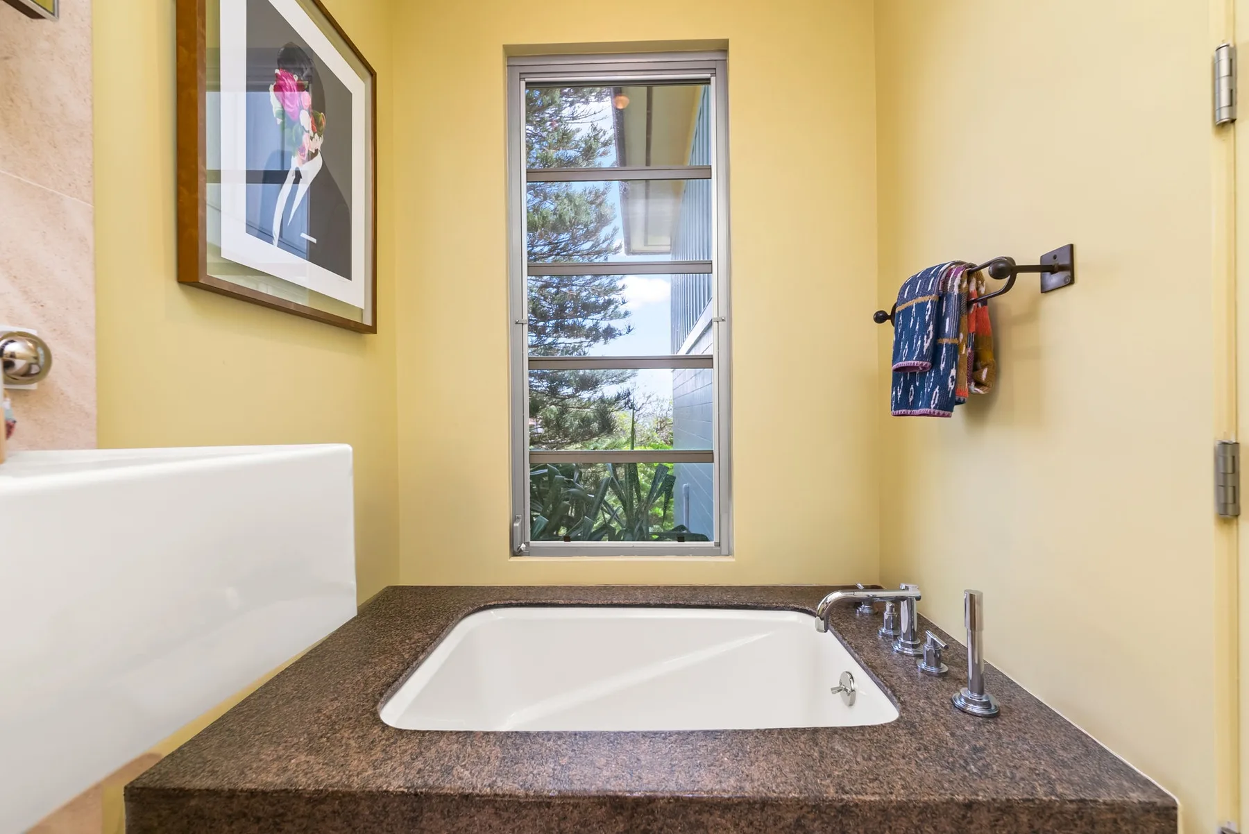 A bathroom with a bathtub beneath a tall window and framed artwork on the wall.