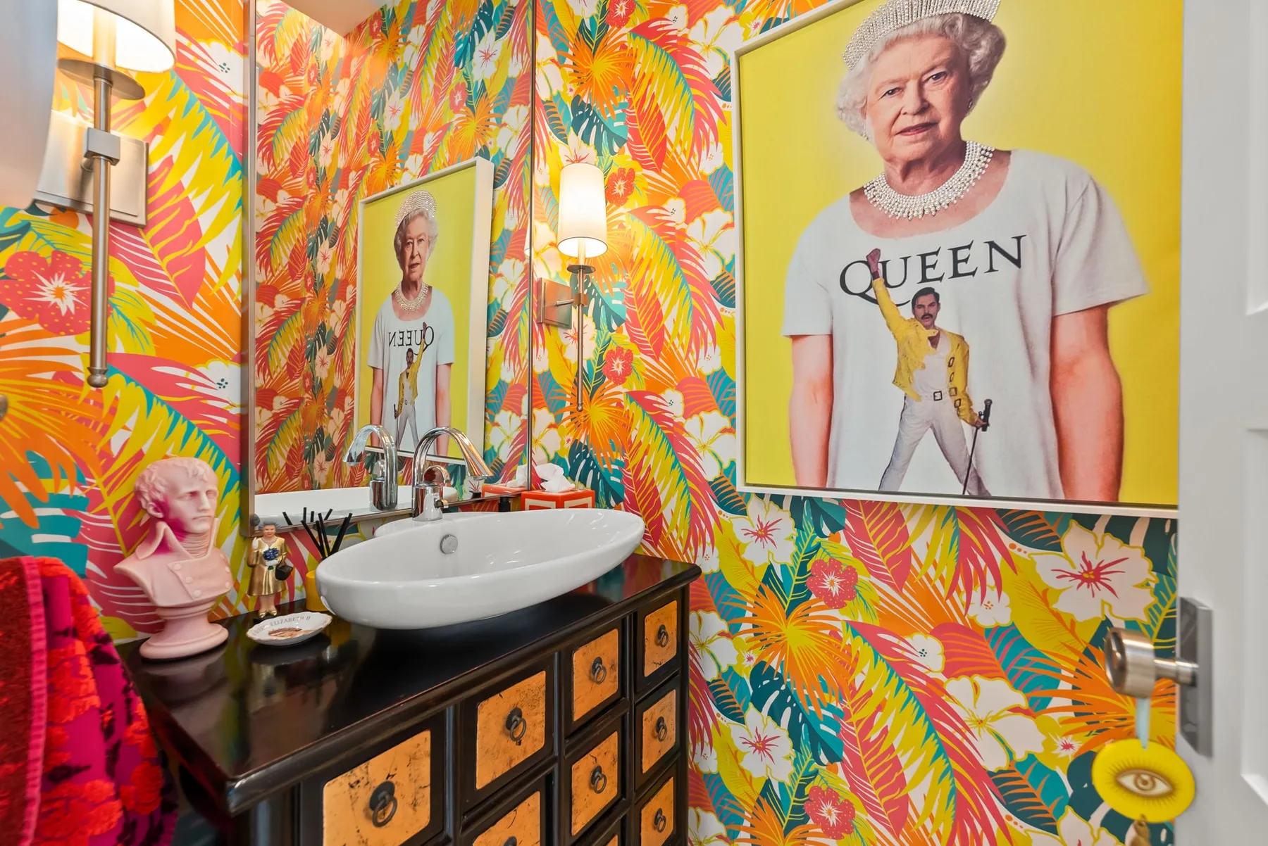 A colorful bathroom vanity stands against bright tropical-patterned wallpaper.