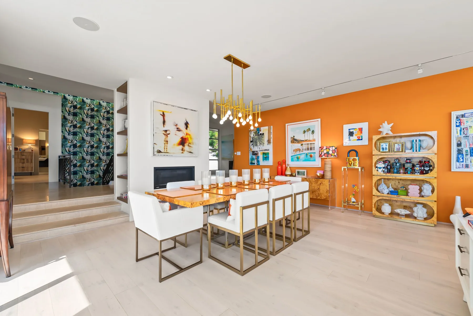 A dining area with a long table, white seating, and an orange accent wall.