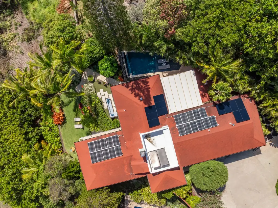 Aerial view of a red-roofed building surrounded by lush greenery, with a pool nearby.