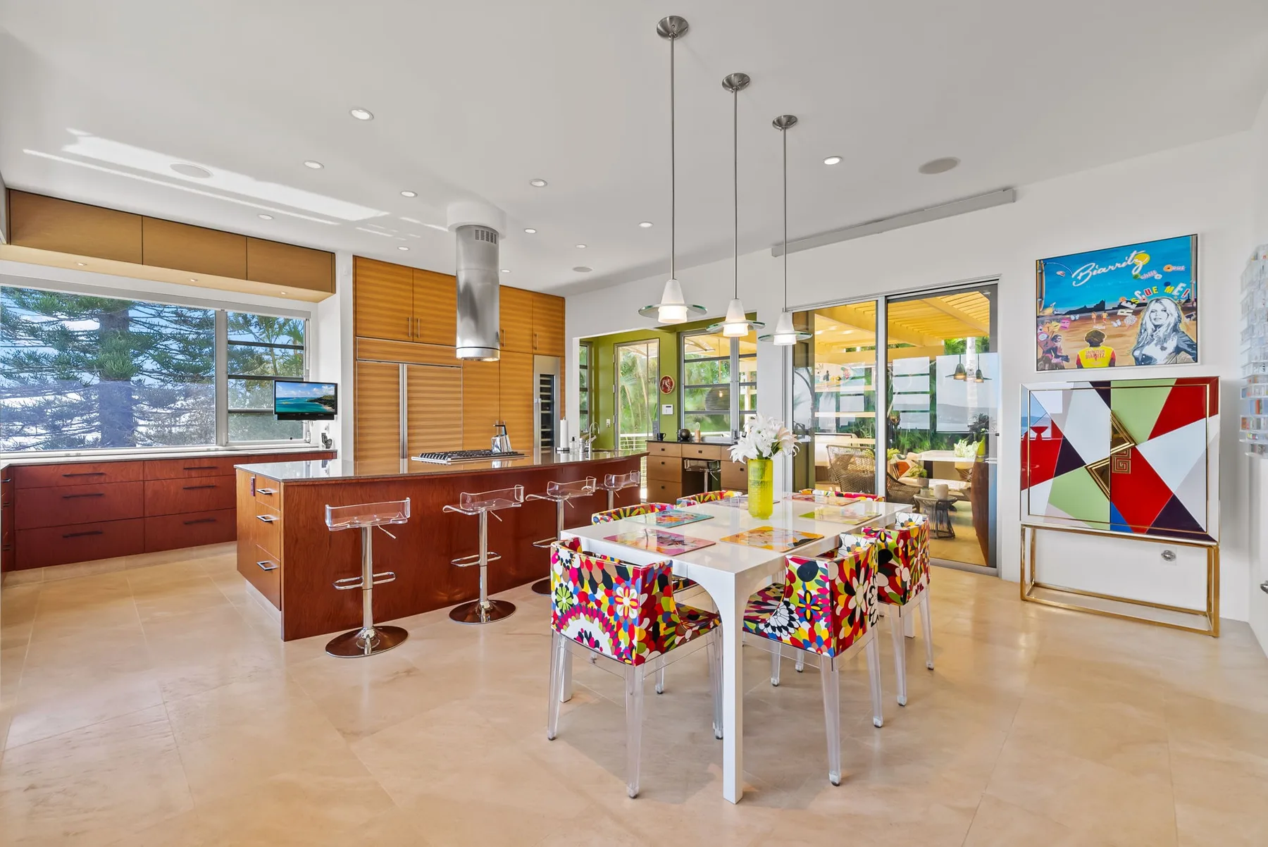 A bright open-plan kitchen and dining area with a colorful table and pendant lights.