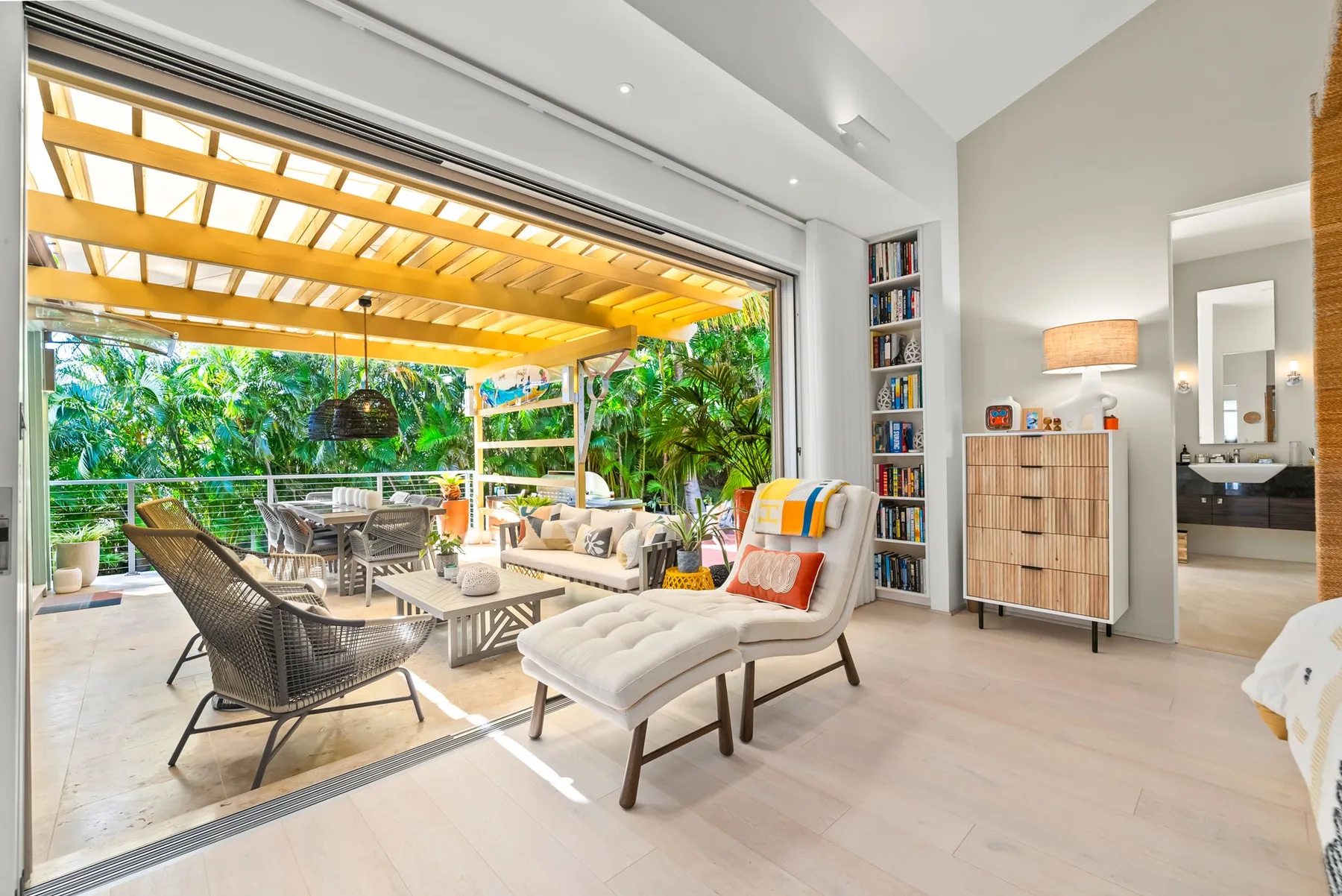 A bright living area opens onto a covered patio with outdoor seating and greenery.
