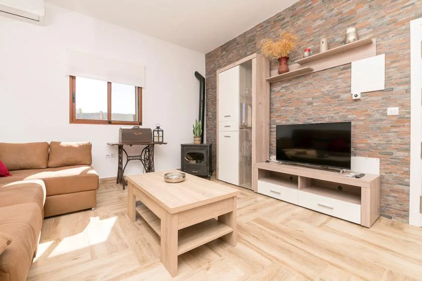 A living room with a sofa, coffee table, and television against a brick-patterned wall.