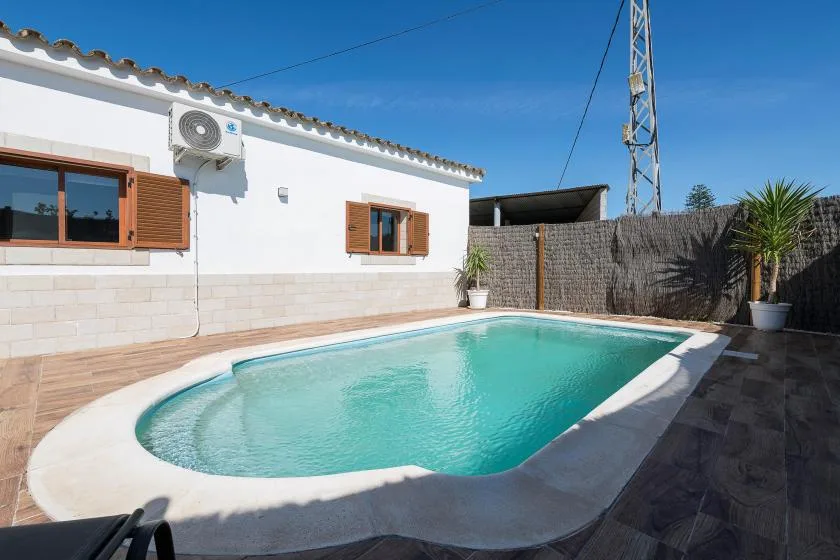 An outdoor swimming pool beside a white building, with potted plants along the fence.